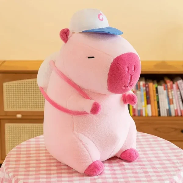 Peluche capybara rose pâle kawaii, casquette "C", sac à dos blanc et duveteux.