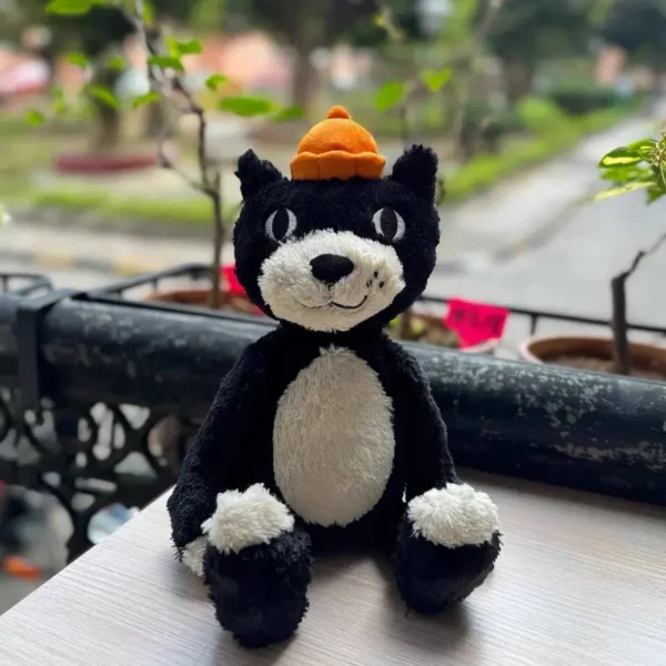 Peluche chat Jellycat noire et blanche 32 cm, bonnet orange vif, douceur premium.